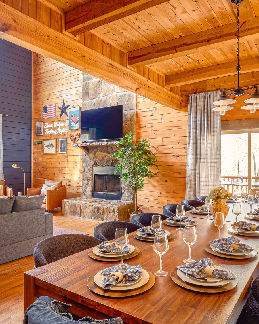 Cabin dining room with a long set table, stone fireplace, and vaulted wood ceilings